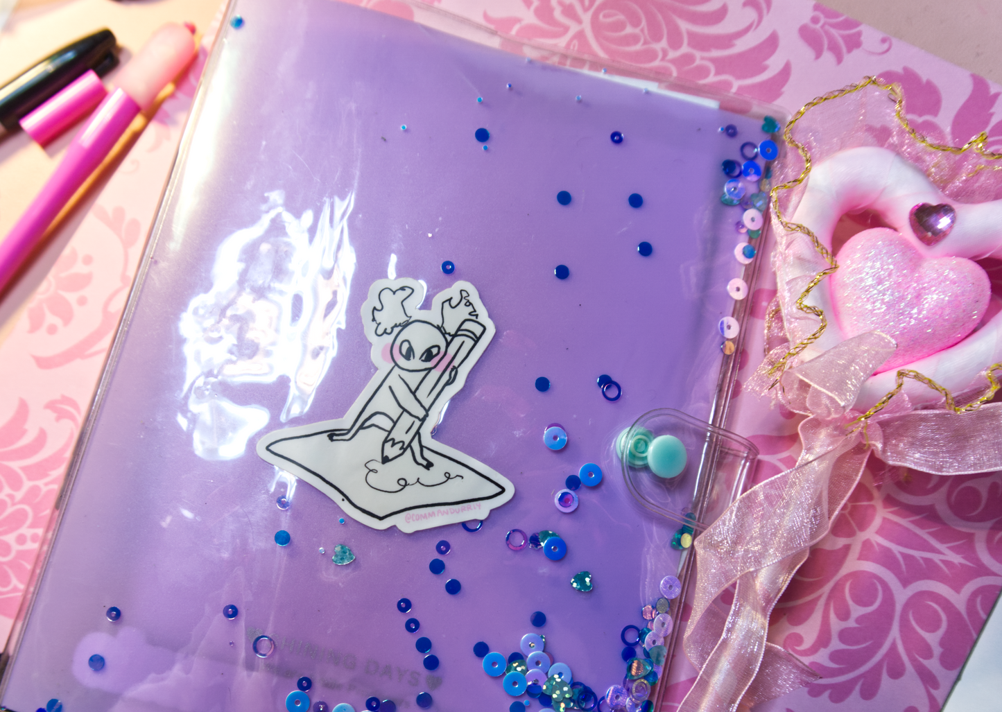 Image of the Busy Busy sticker, placed on a planner next to a pink heart pen.