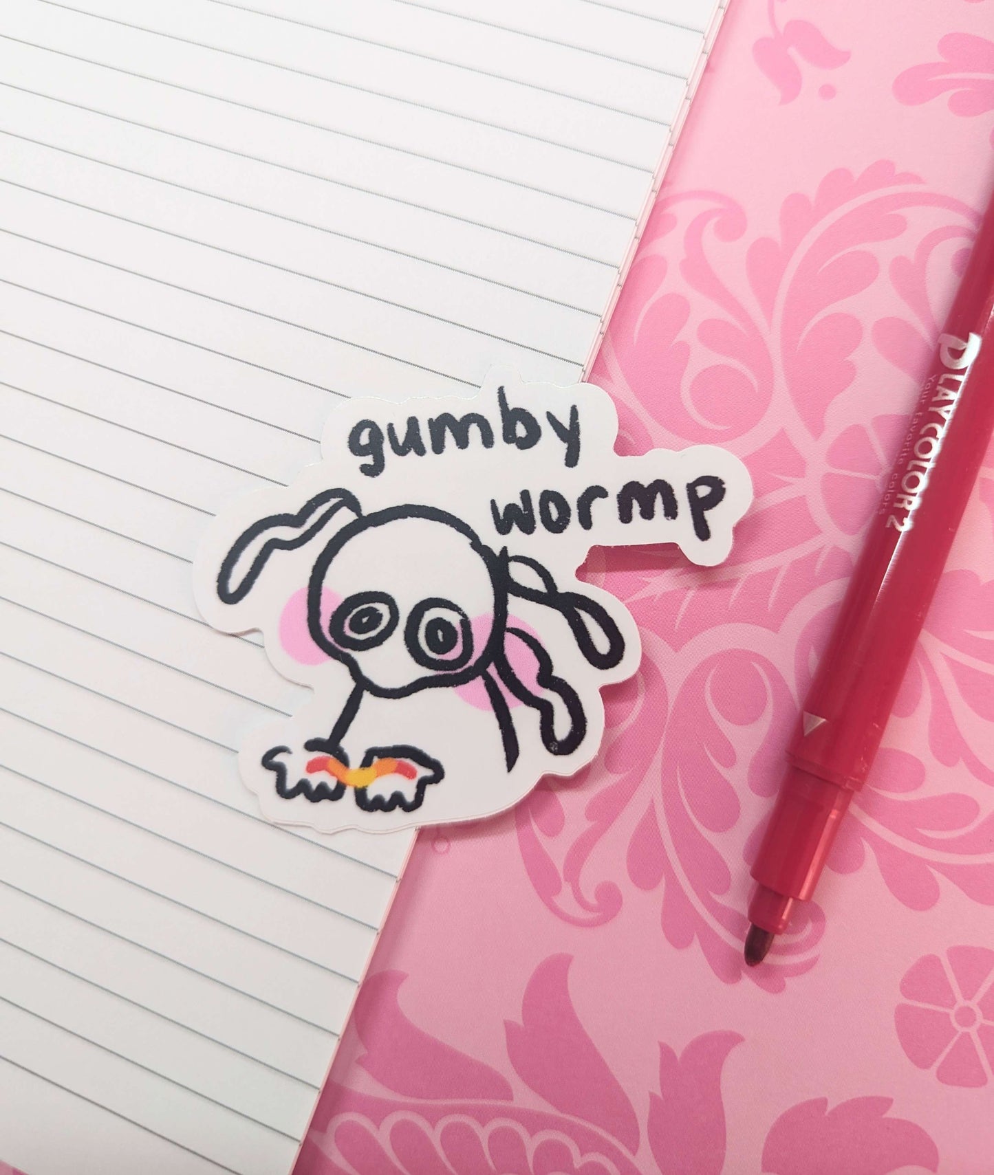 A sticker featuring a cute character gently holding a colorful gummy worm in the palms of their hands. Text above it reads, 'gumby wormp.'