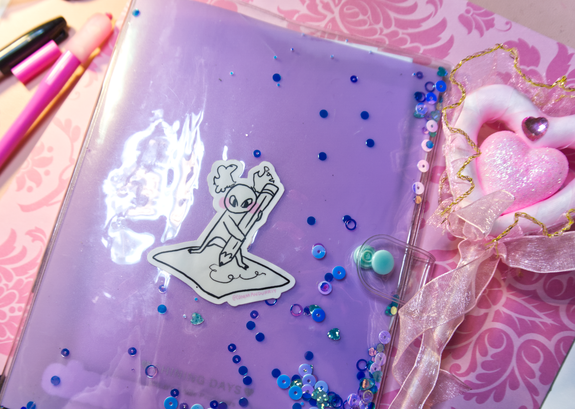 Image of the Busy Busy sticker, placed on a planner next to a pink heart pen. 