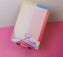 Load image into Gallery viewer, Notepad on a stand, sitting at an angle in front of a pink and white background.
